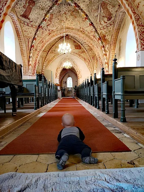 Baby krabbelt auf rotem Teppich in Kirche.