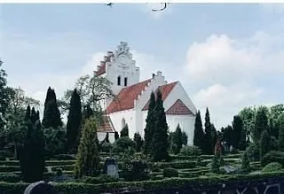 Weiße Kirche mit rotem Dach und Friedhof.